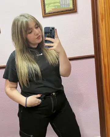 Laura, de Centro Ónix, de pie con camiseta y vaqueros negros, haciéndose una foto con el móvil