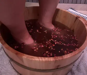 Pies dentro del barreño de madera con agua y pétalos secos de rosa