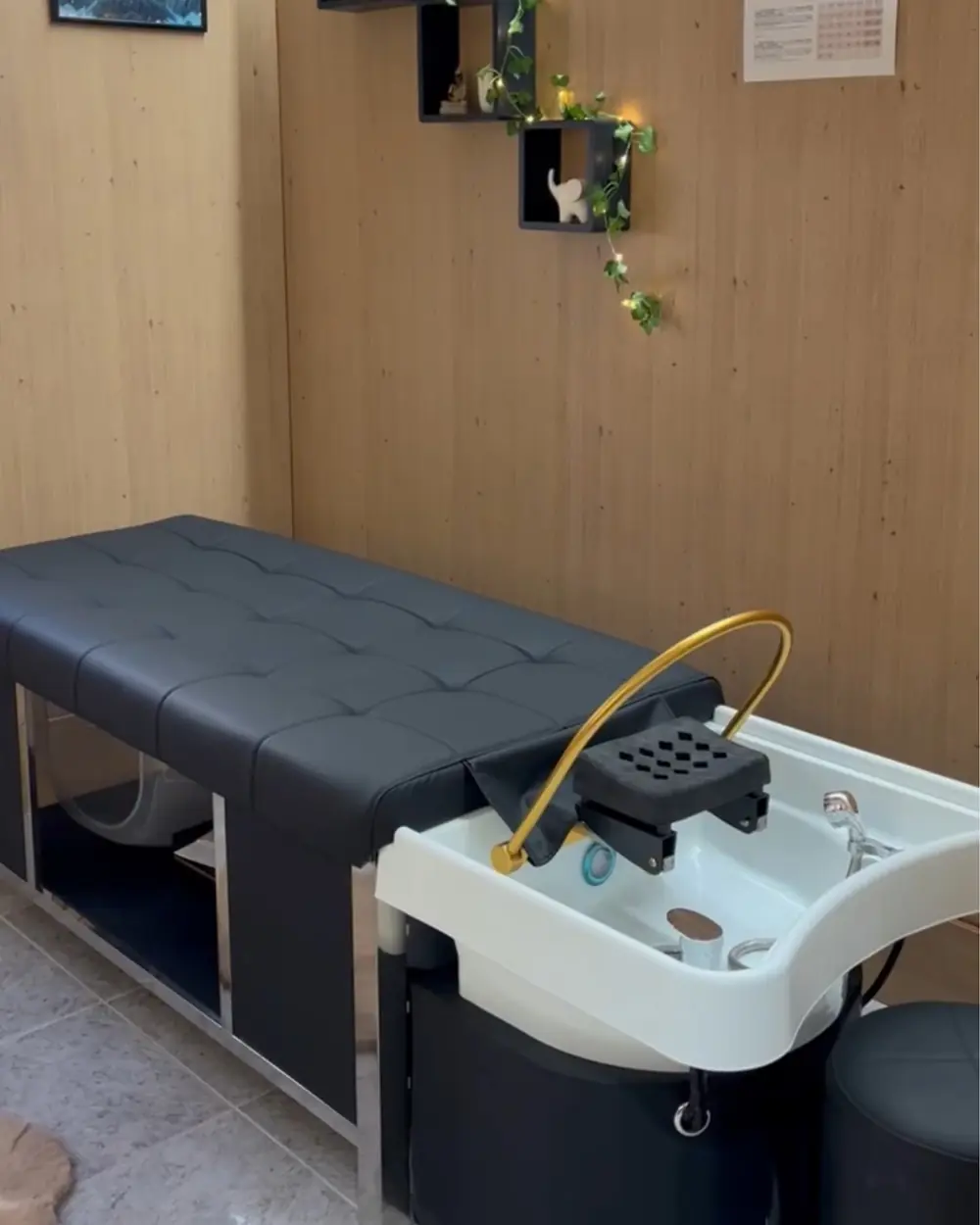 Lavacabezas negro con brazo dorado del spa capilar, junto a una pared de madera clara