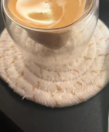Vaso de cristal con café y espuma sobre un posavasos de cuerda, la bebida de cortesía del spa capilar